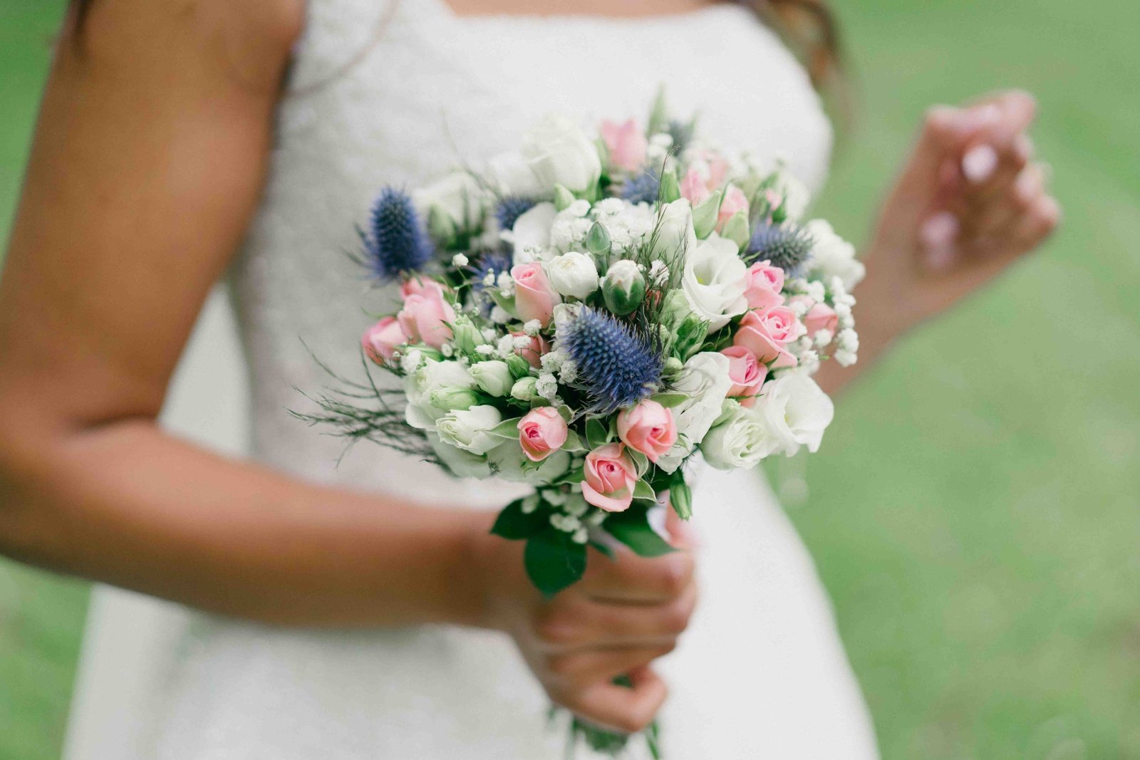 Détail mariée tenant son bouquet de roses pastel et chardons bleus dans un jardin, photographe mariage Cyril Steau